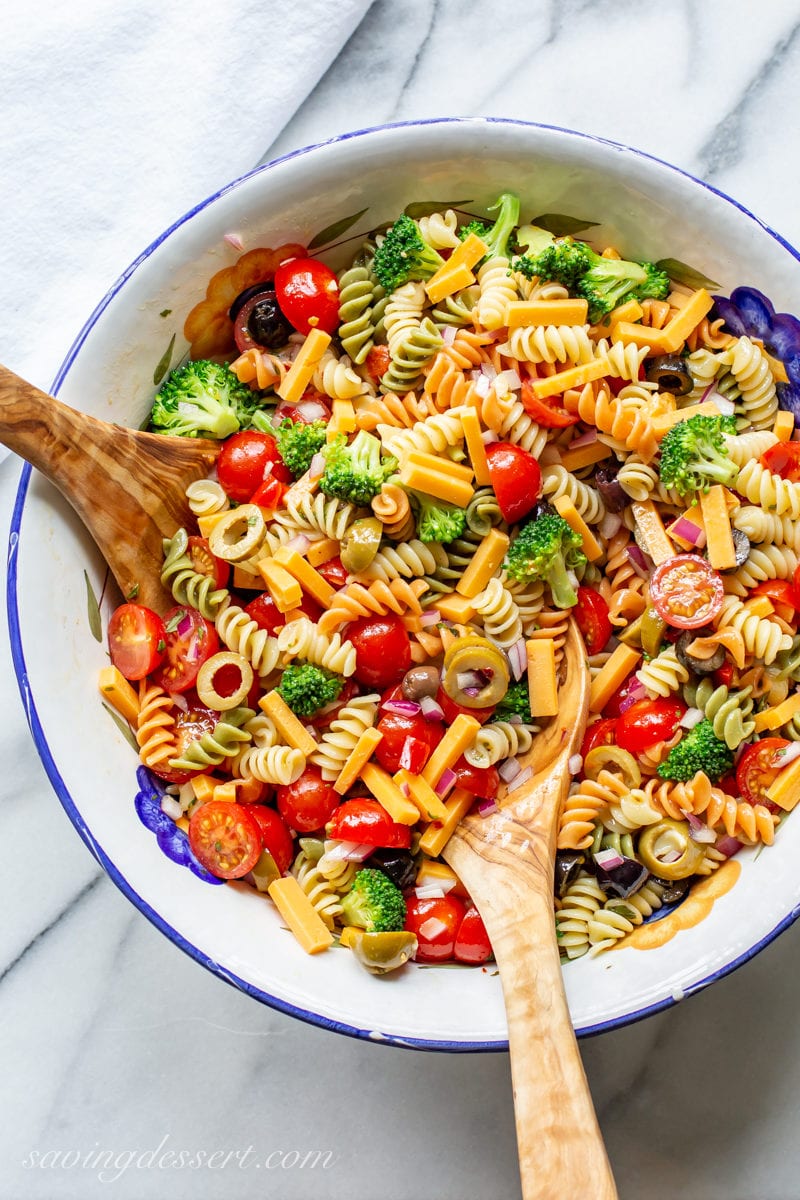 A bowl of pasta salad with cheese, olives, tomatoes, broccoli and spiral noodles tossed in a zesty Italian dressing