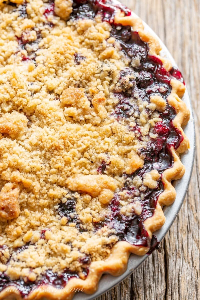 A blueberry crumble pie with juices bubbling over the edge of the pie crust