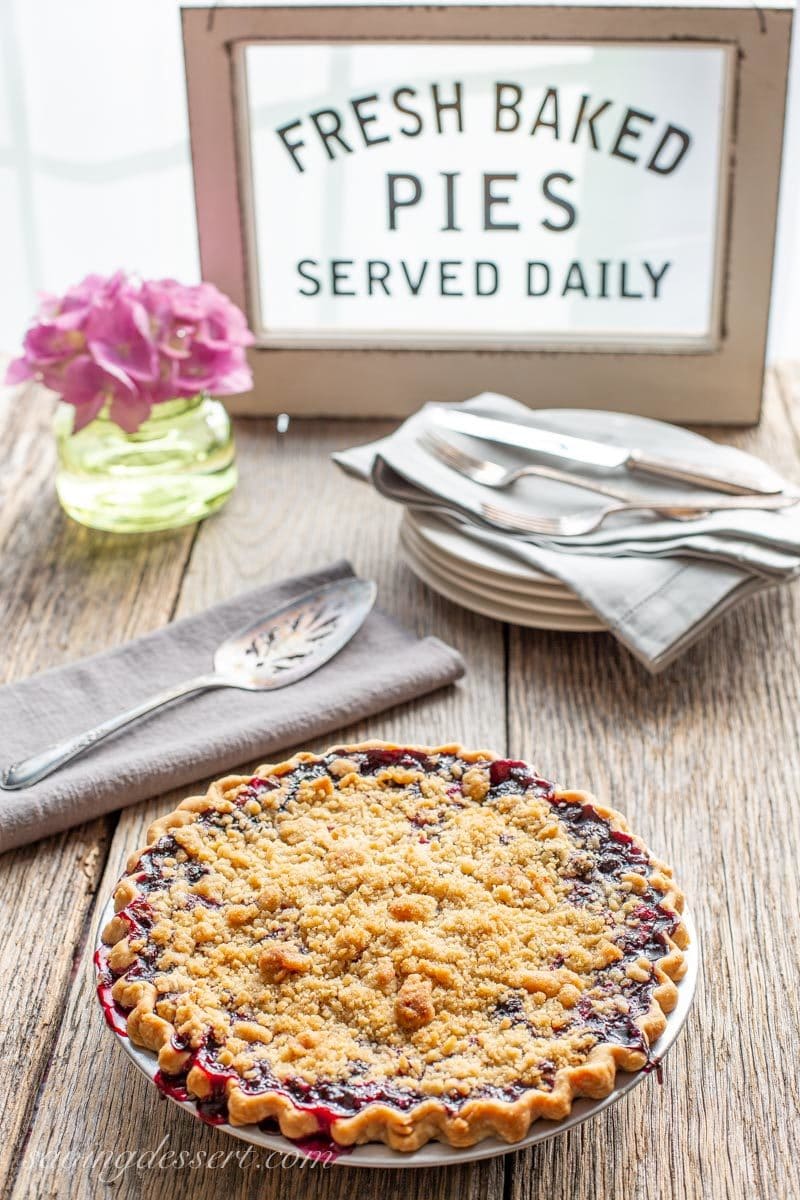 blueberry crumble pie on a table with a spatula, plates and forks