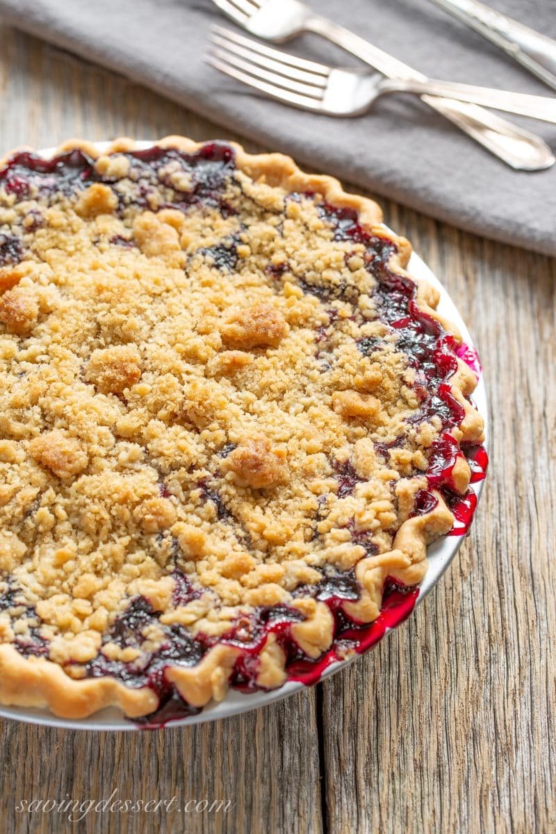 A blueberry pie with a crumble top, baked to a golden brown with juices overflowing the pan