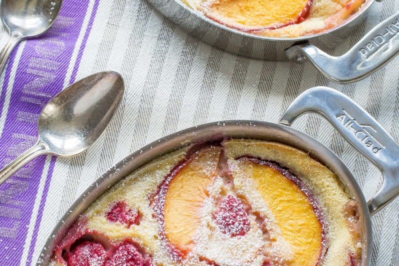 An overhead shot of two small casseroles filled with a peach and raspberry clafoutis
