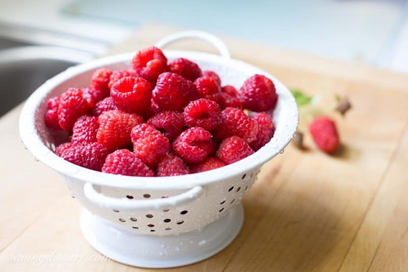 A bowl of fresh raspberries on a cutting board.