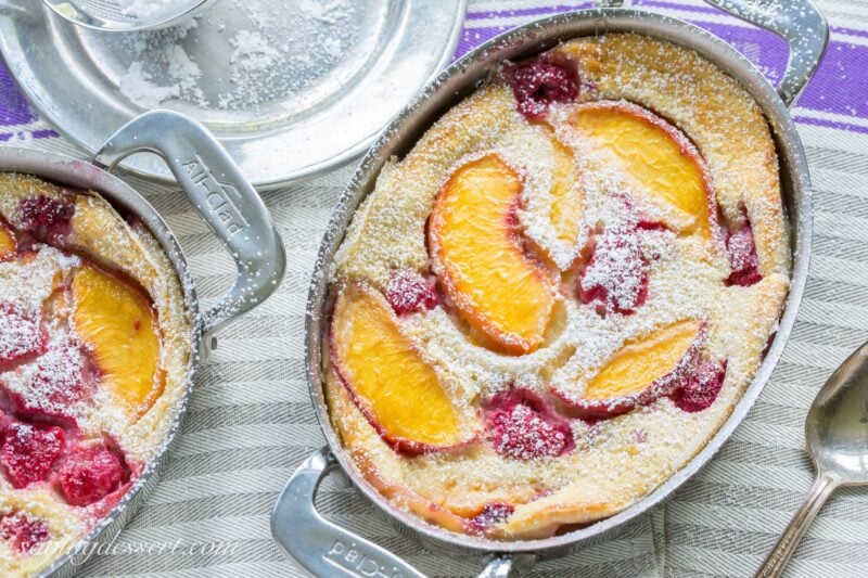 A small casserole with raspberry peach clafoutis dusted with powdered sugar
