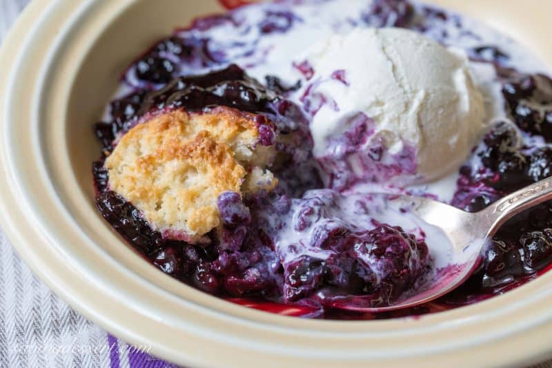 A closeup of a bowl of black raspberry cobbler topped with a scoop of ice cream