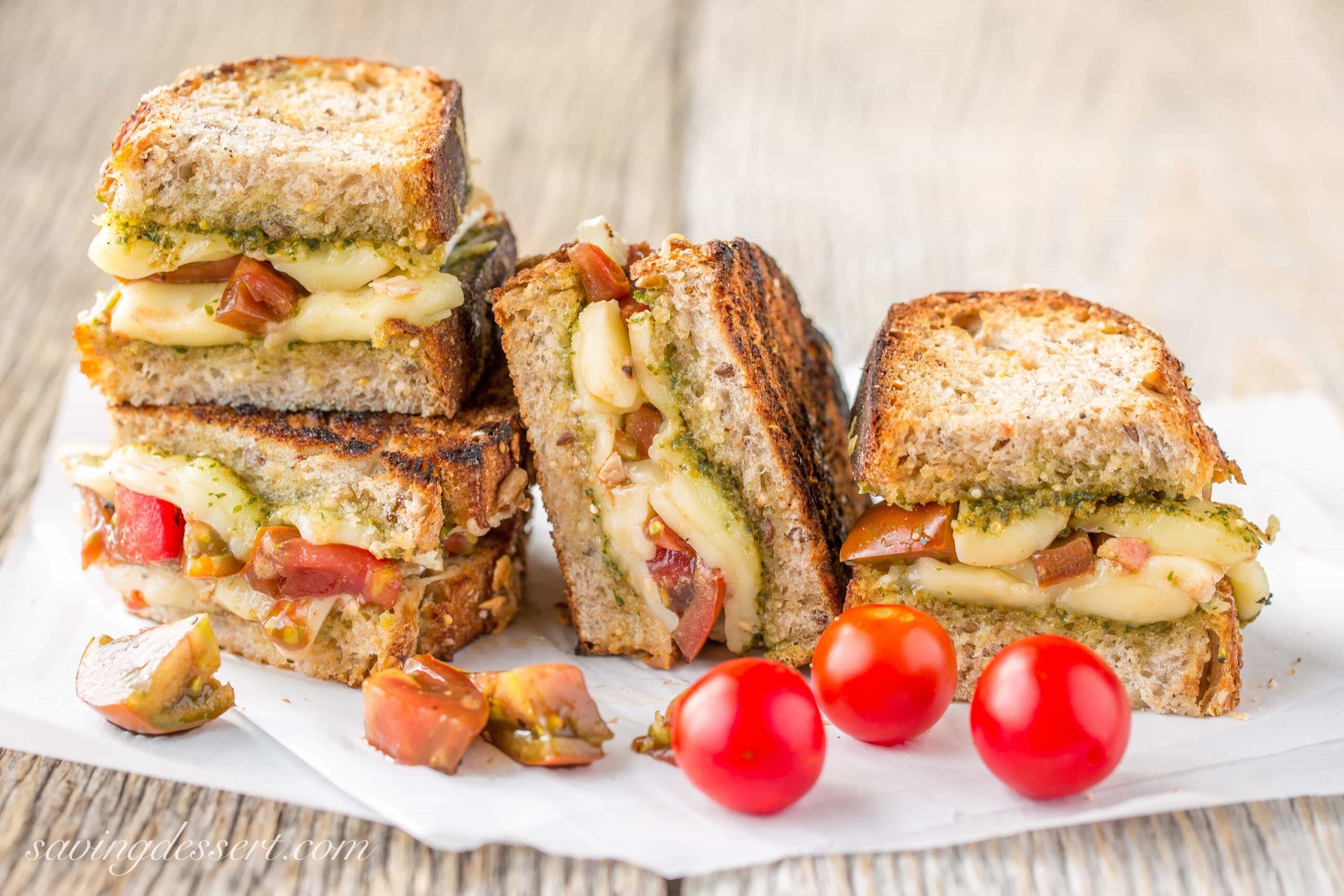 A grilled cheese sandwich with tomatoes on a cutting board.