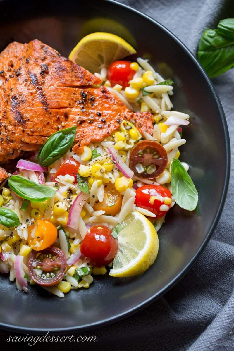 A bowl of grilled salmon with an orzo corn salad and fresh herbs