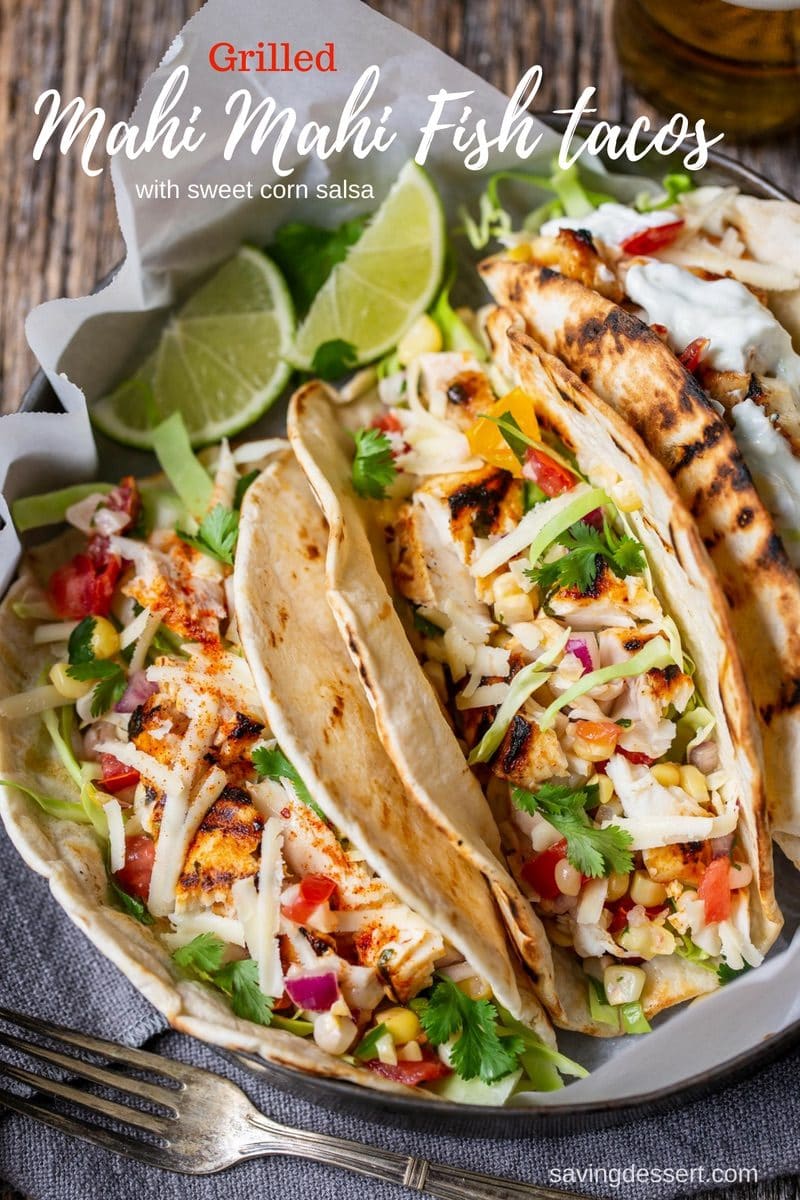 A pan of fish tacos topping with sweet corn salsa, cabbage and lime wedges