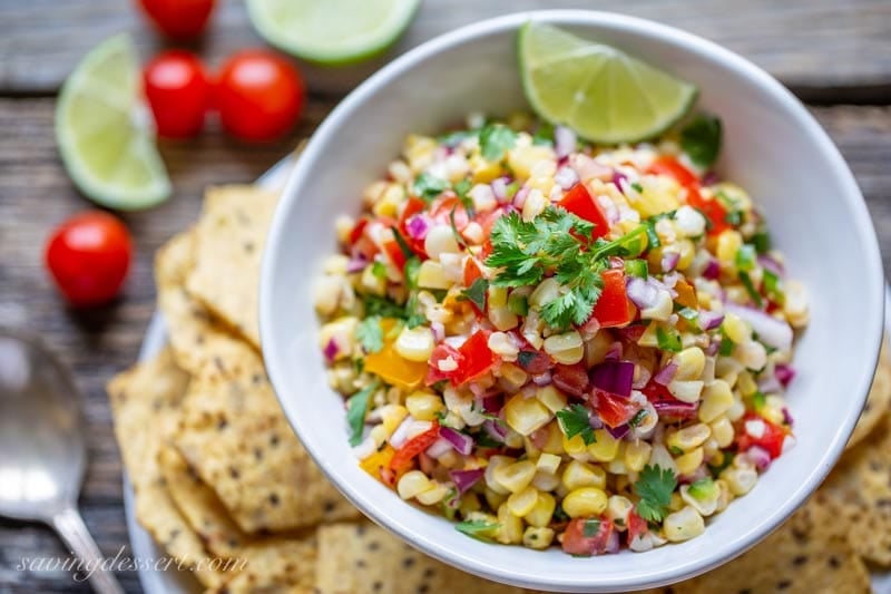 A bowl of sweet corn salsa with chips and lime wedges.