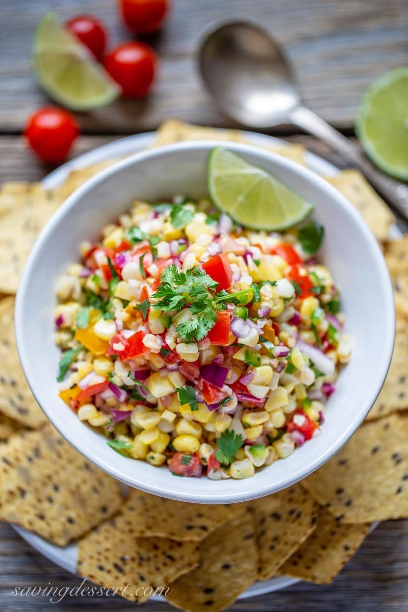 A bowl of fresh corn salsa with chips and lime wedges