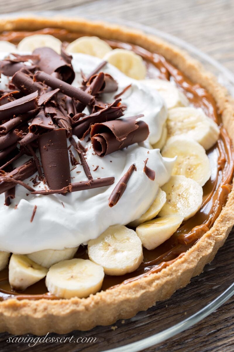 A banoffee pie with a cookie crust, smooth caramel filling, topped with sliced bananas, whipped cream and chocolate curls