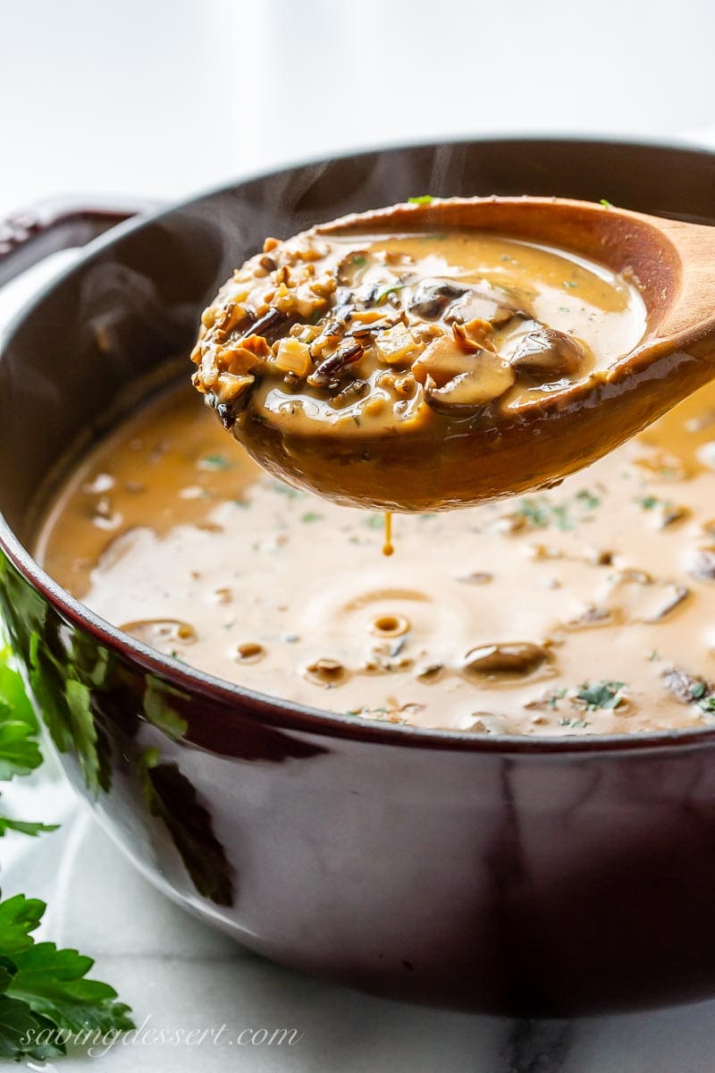 A ladle filled with golden hued soup over a Dutch oven