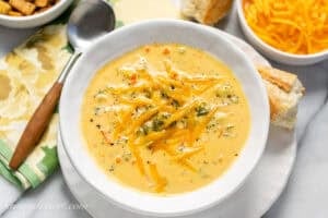 A bowl of broccoli cheddar soup with extra cheddar, bread and croutons on the side.
