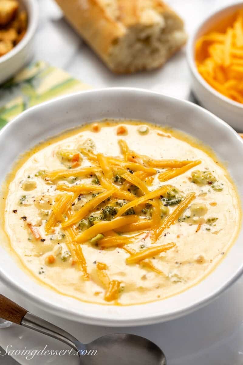 A bowl of cheesy broccoli cheddar soup with bread on the side.