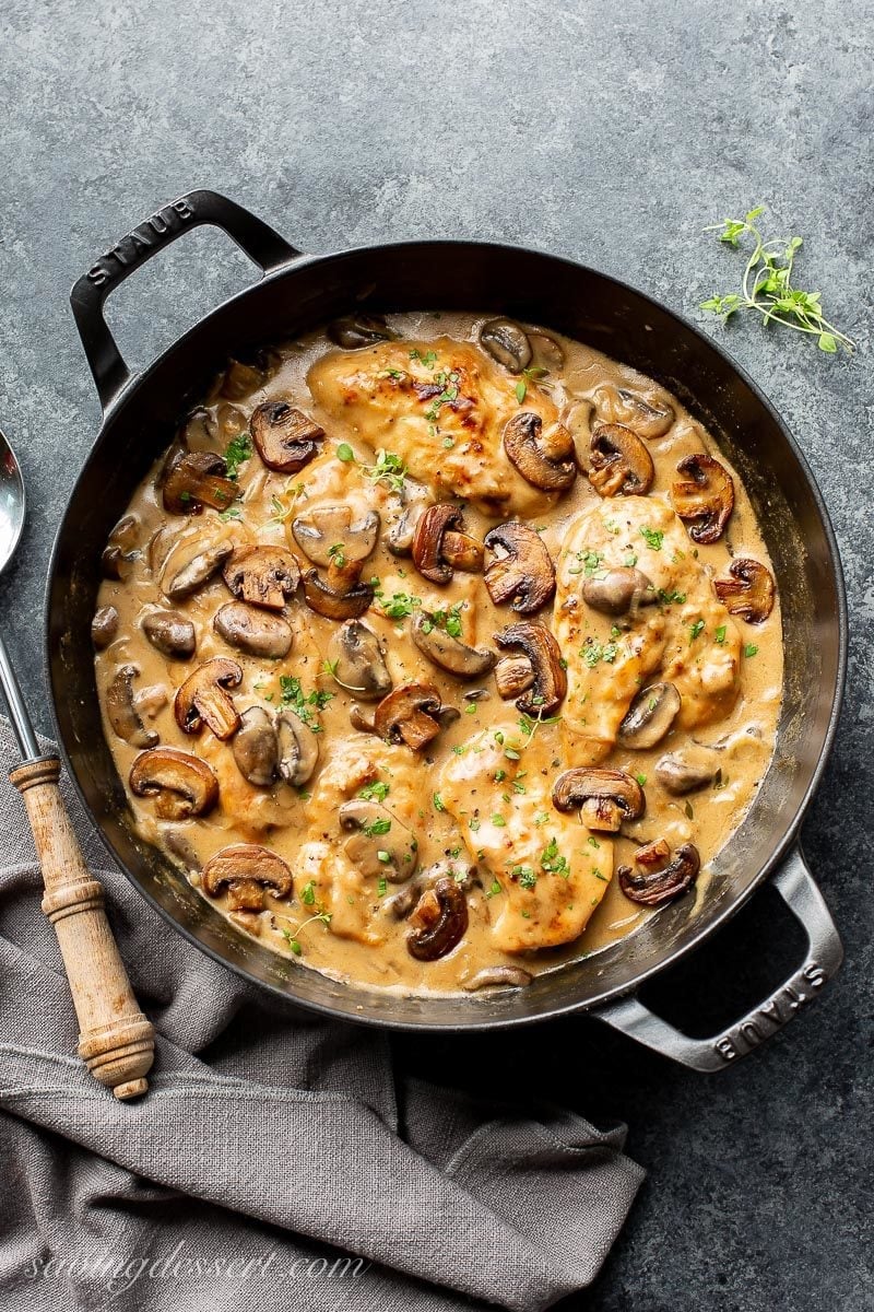 A skillet with chicken and mushrooms with fresh thyme