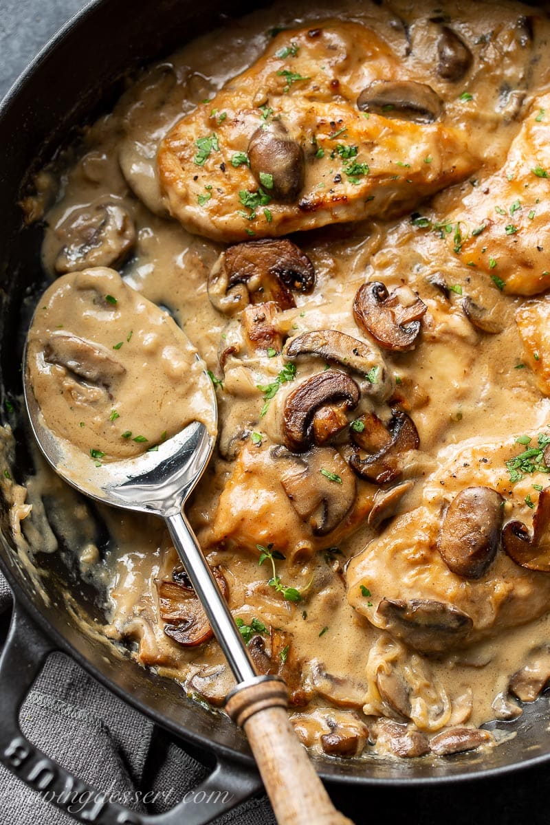 A skillet filled with chicken breasts, with mushrooms and gravy
