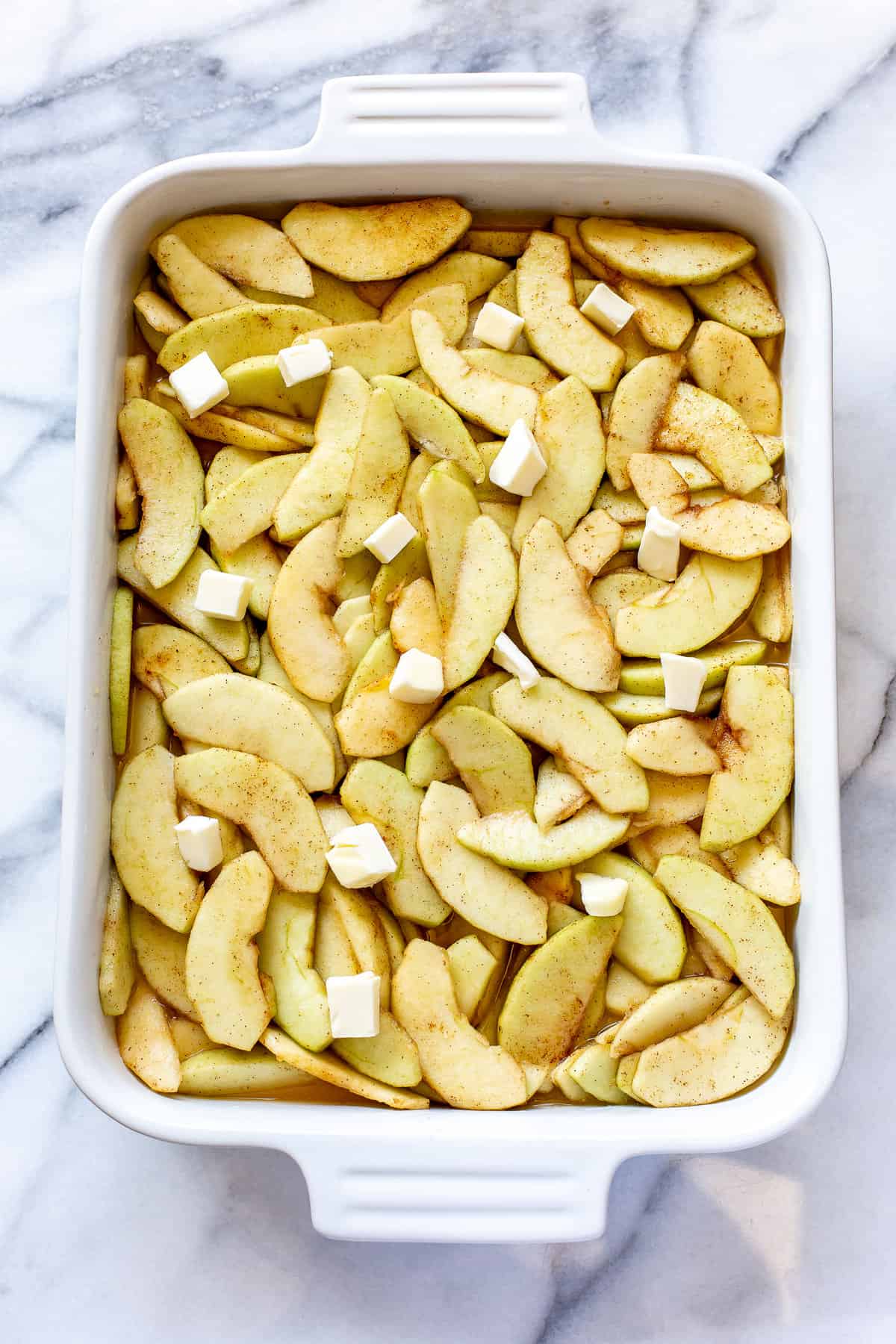 A casserole dish filled with apples, apple cider and small chunks of butter