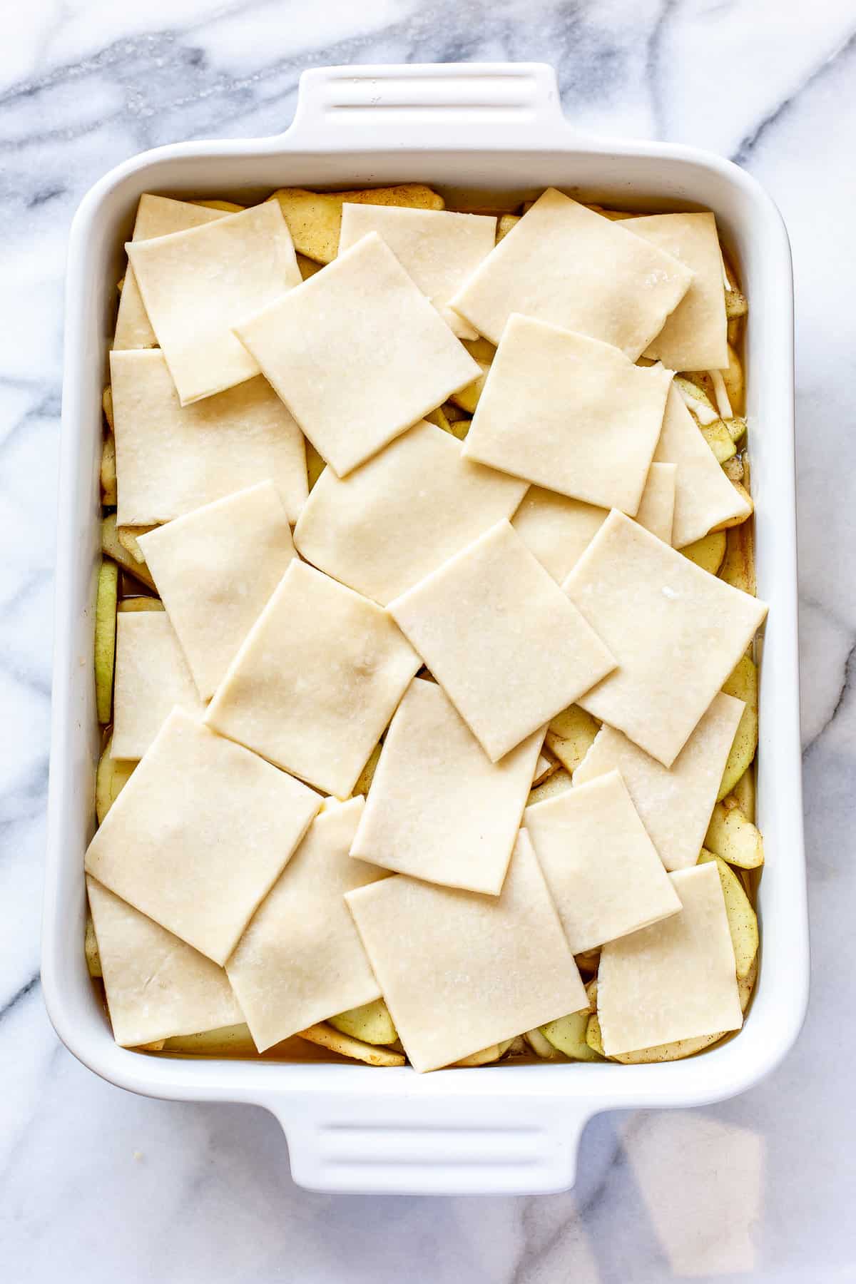 Apple filling in a casserole dish topped with squares of buttery pie pastry in a patchwork design