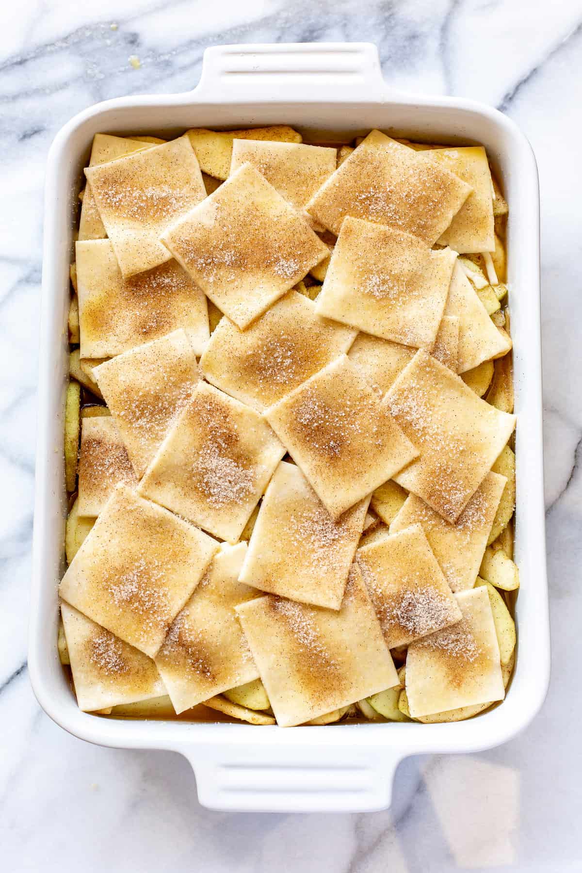 A photo showing squares of pastry dough sprinkled with cinnamon and sugar on top of a apple filling