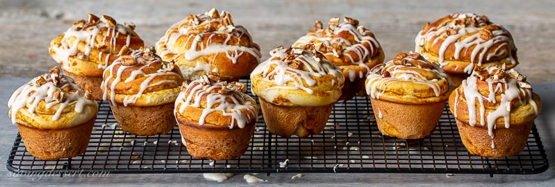 A cooling rack filled with cinnamon rolls drizzled with icing and chopped pecans