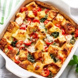 An overhead view of a breakfast strata in a square casserole dish with fresh basil on the side and on top.