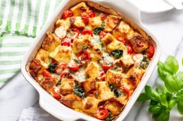 An overhead view of a breakfast strata in a square casserole dish with fresh basil on the side and on top.