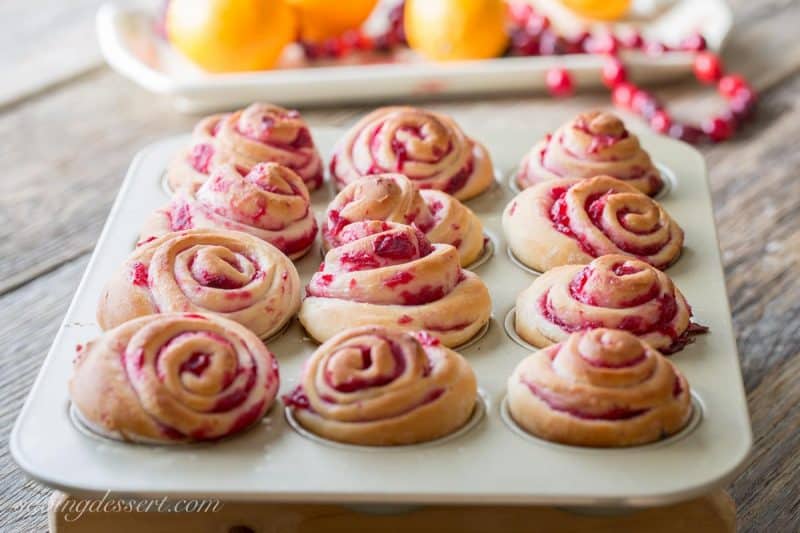 Cranberry Swirl Buns in a muffin tin with fresh oranges and cranberries