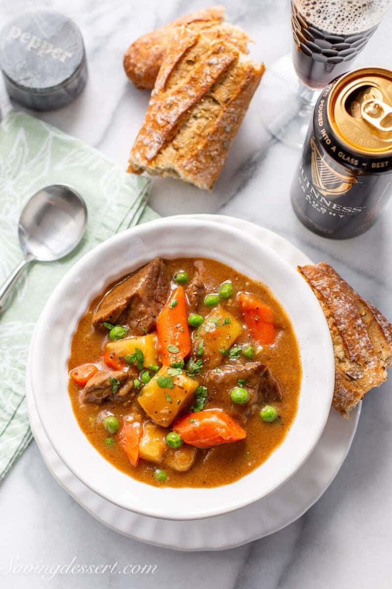 A bowl of Guinness Beef Stew with a baguette for dipping and a Guinness Beer.