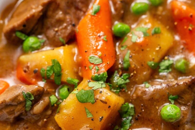 An overhead view of a bowl of beef stew with peas, potatoes and carrots.
