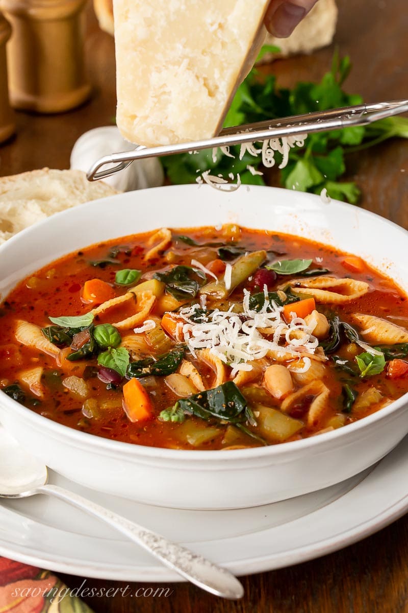 A large bowl of Minestrone Soup with Parmesan cheese being grated over the top