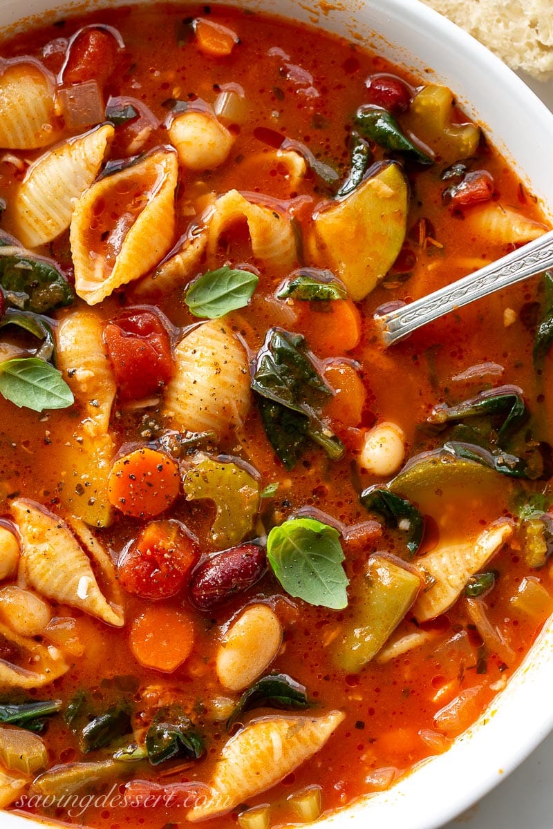 A hearty bowl of vegetable soup with shell shaped pasta, basil leaves and spinach