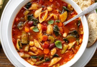 A close up of a bowl of Minestrone Soup with spinach and fresh basil leaves