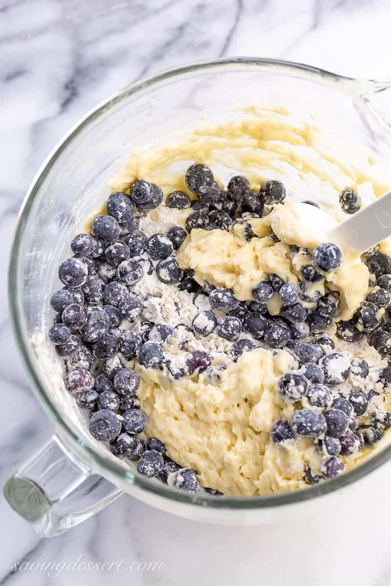 A bowl of batter with flour and blueberries being folded in