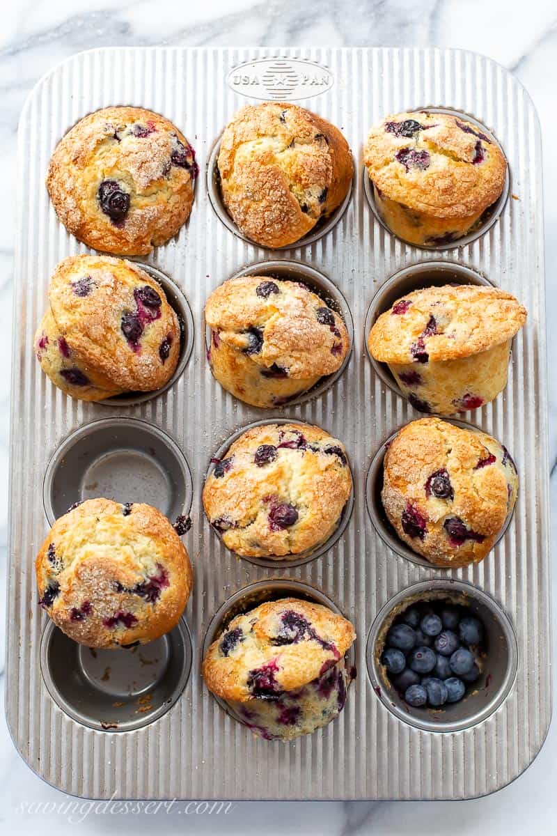 A muffin tin with baked blueberry muffins cooling