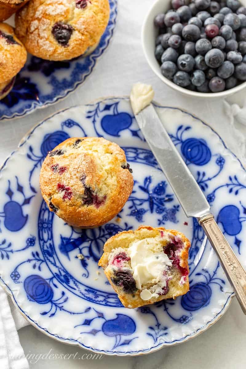 Blueberry muffins on a plate with a knife with butter, a bowl of fresh blueberries