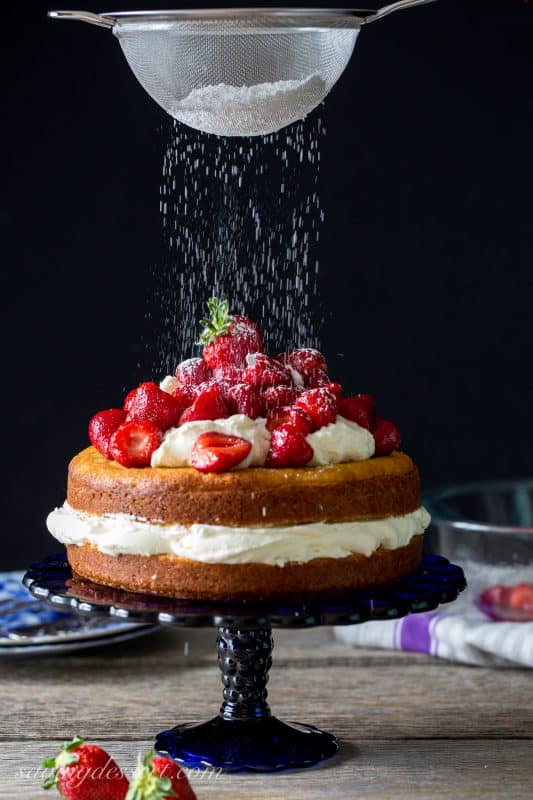 A fresh Strawberry Mascarpone Cake being dusted with powdered sugar