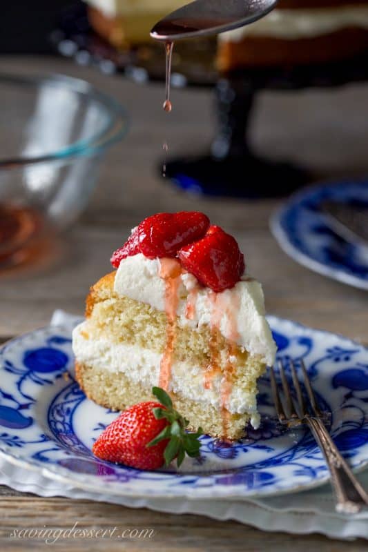 A slice of Strawberry Mascarpone Cake on a plate being drizzled with strawberry syrup