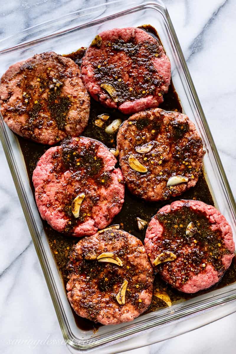 A glass casserole dish with uncooked hamburgers in a marinade