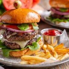 A double decker hamburger on a toasted bun with cheese, onions, tomato and lettuce