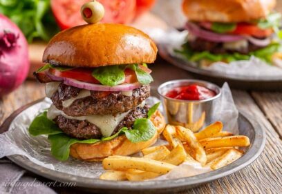 A double decker hamburger on a toasted bun with cheese, onions, tomato and lettuce