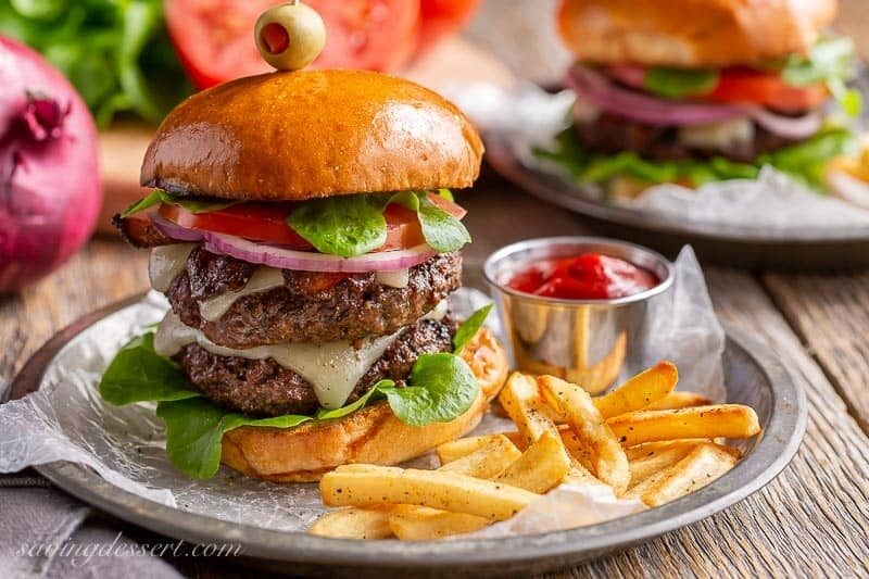 A double decker hamburger on a toasted bun with cheese, onions, tomato and lettuce