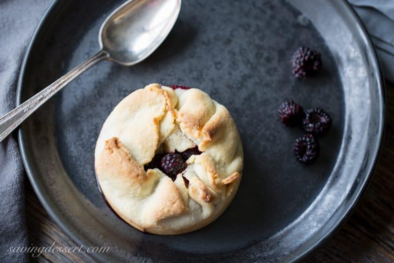 A mini deep dish berry pie on a plate with black raspberries