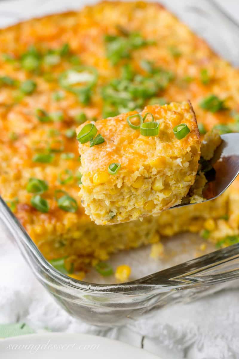 A piece of cheesy corn casserole on a spatula topped with sliced green onions