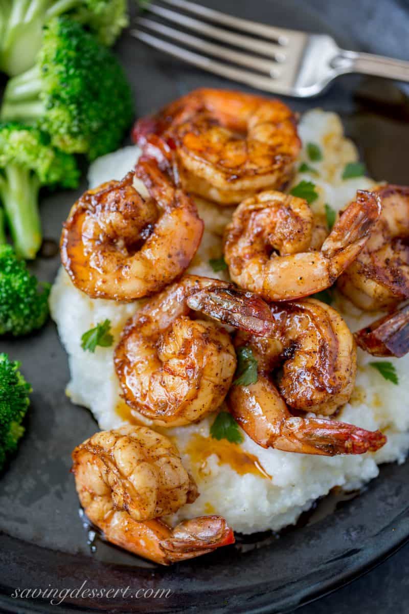 A plate of grits and broccoli topped with spicy chili garlic shrimp
