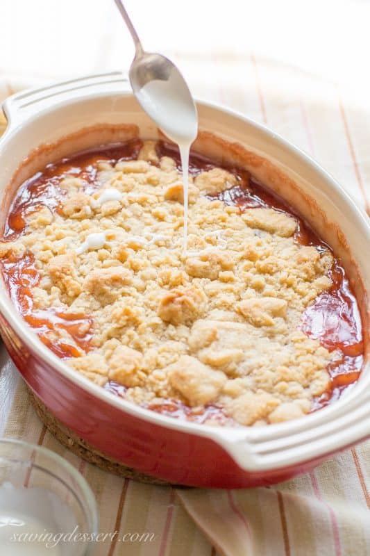 A casserole dish filled with a peach crumble drizzled with a simple icing