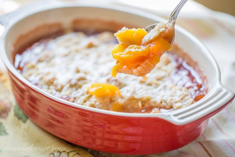 A spoonful of peach crumble over a casserole dish