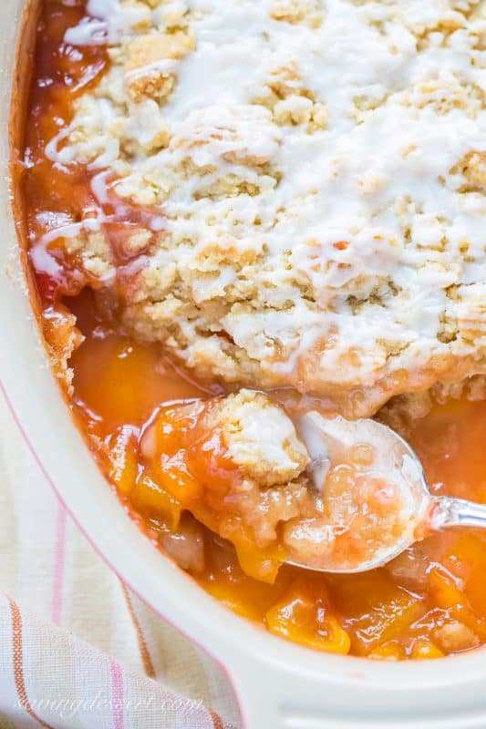 An overhead view of a casserole dish filled with a peach crumble with a spoon