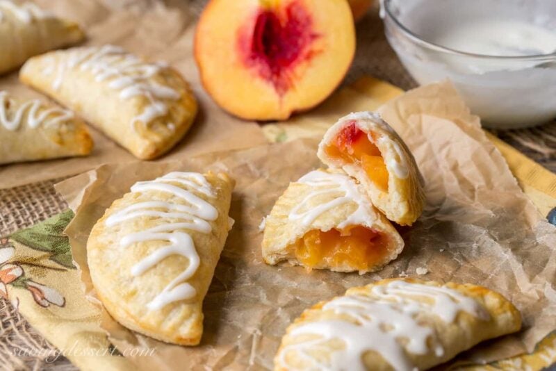 A few hand pies on parchment paper with one broken in half revealing a pretty peach filling