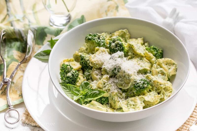 A bowl of tortellini tossed in a basil cream sauce and garnished with Parmesan and basil leaves