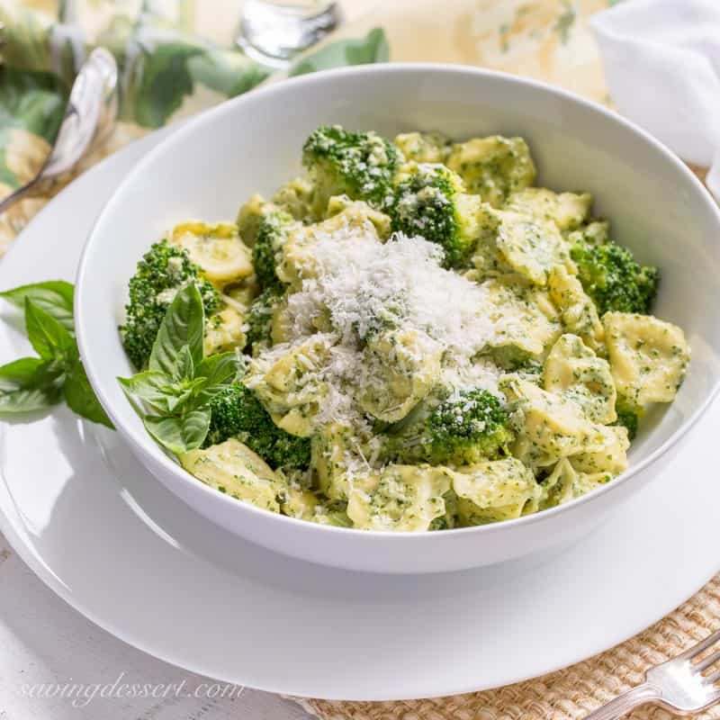 A side view of a bowl of tortellini with broccoli and basil cream sauce topped with Parmesan