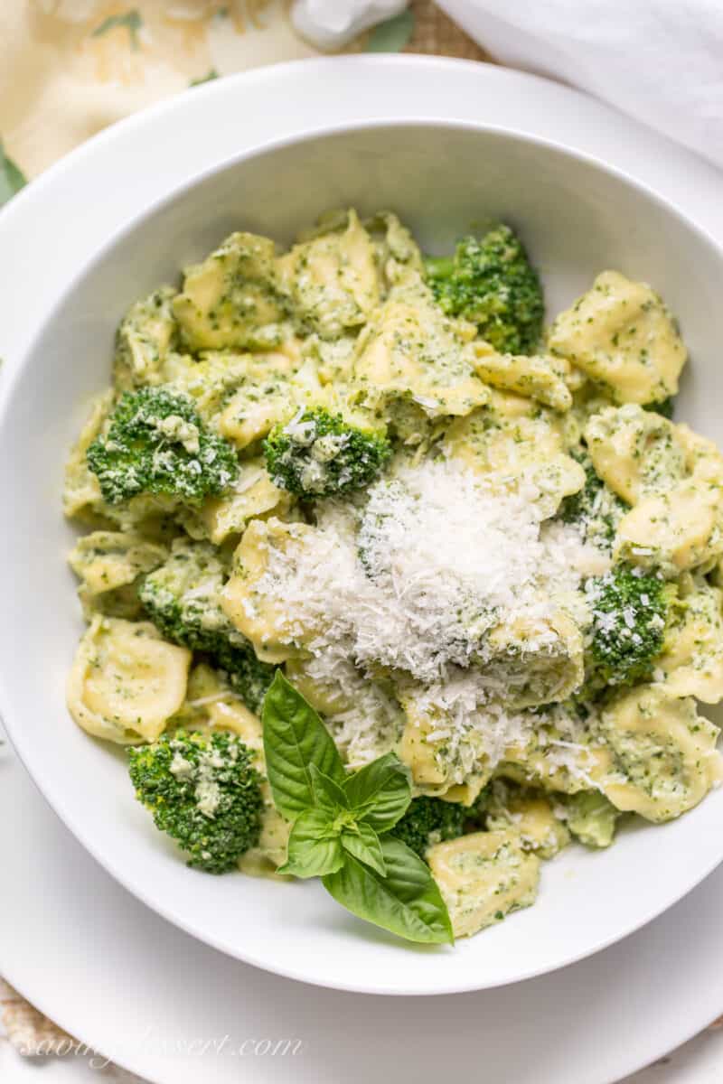 A bowl of tortellini tossed in basil cream sauce and topped with Parmesan